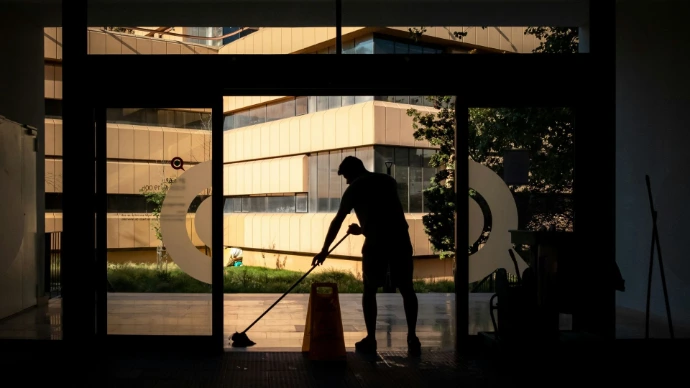 Silhouette d'un agent de propreté effectuant un nettoyage au sol à l'entrée d'un bâtiment moderne, soulignant les conditions de travail, la valorisation du personnel et la performance globale (RSE).