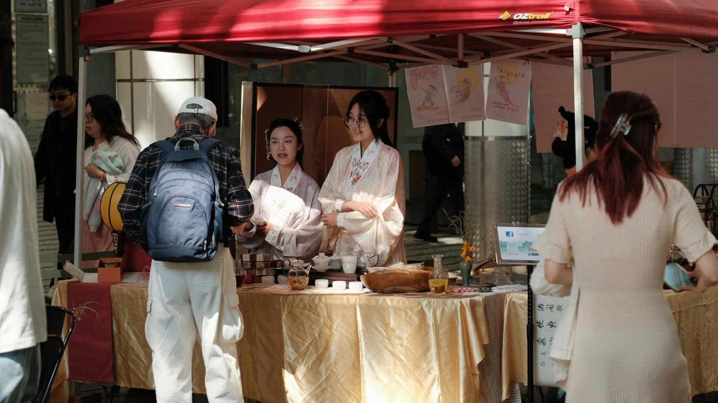 Deux femmes en tenues traditionnelles sourient derrière un stand de thé sous une tonnelle rouge, représentant le développement local.